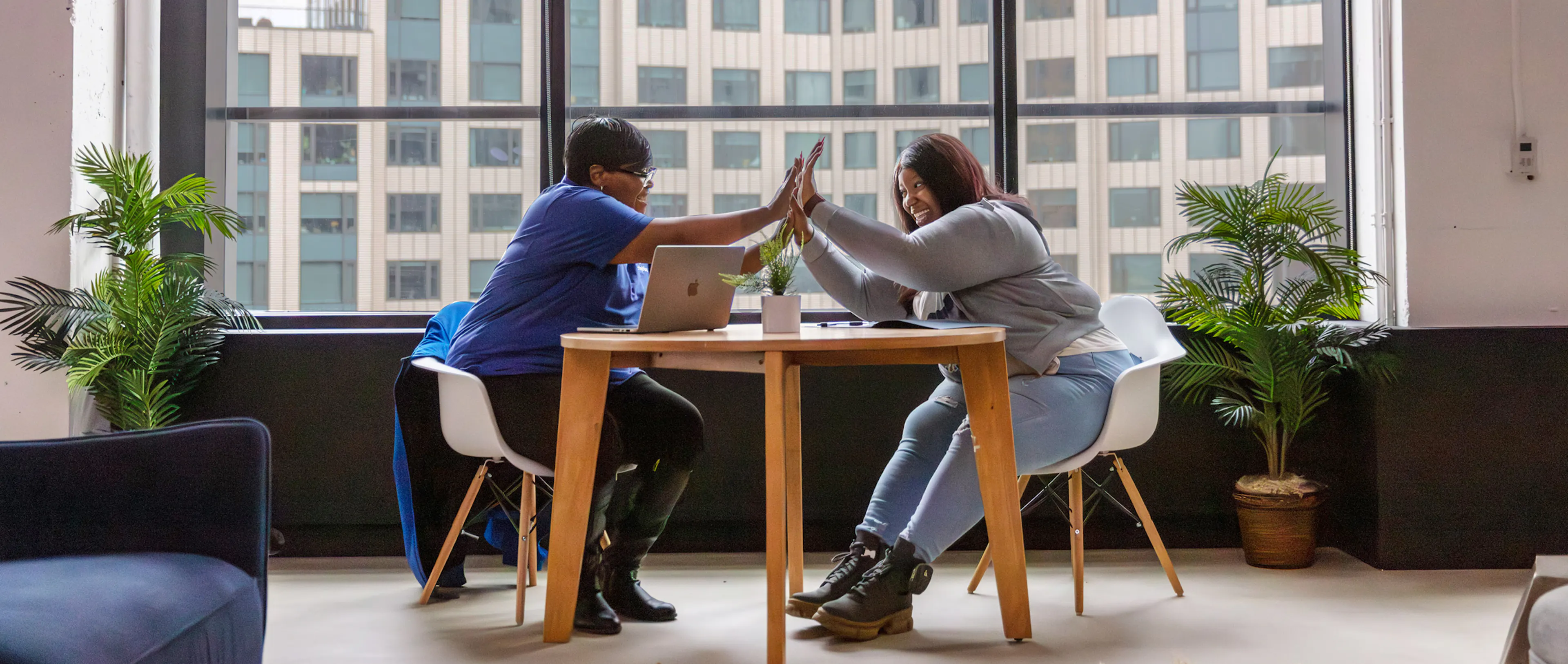 Photo of a community health partner and member sitting at a round table, smiling and giving each other a high-five over an open laptop computer.