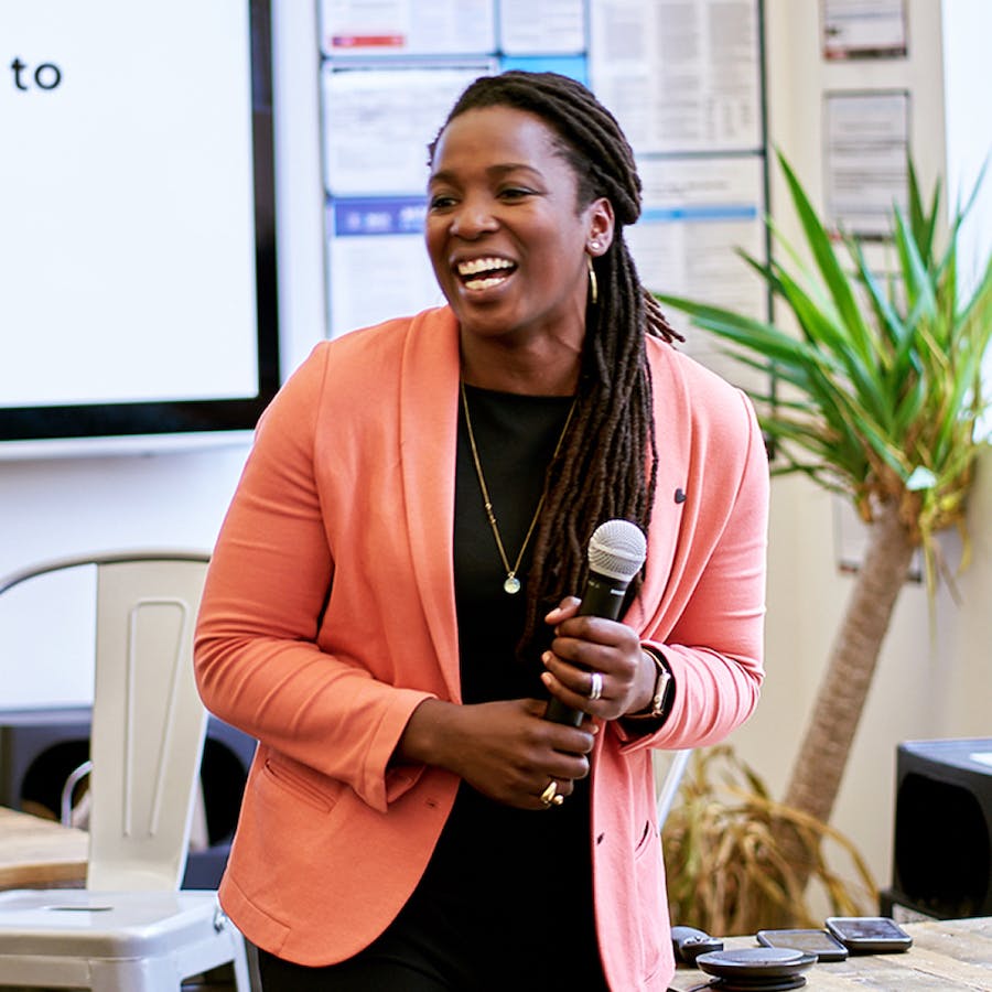 Cityblock Health CEO, Dr. Toyin Ajayi, smiles wearing a coral color blazer while holding a microphone