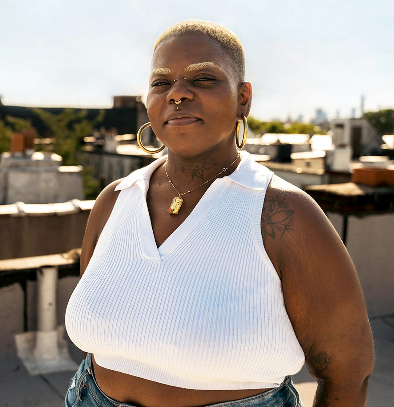 Woman with blonde hair and eyebrows  wearing a white top smiles proudly on a New York rooftop.