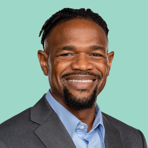 Man smiles proudly wearing a blue button down and gray jacket.