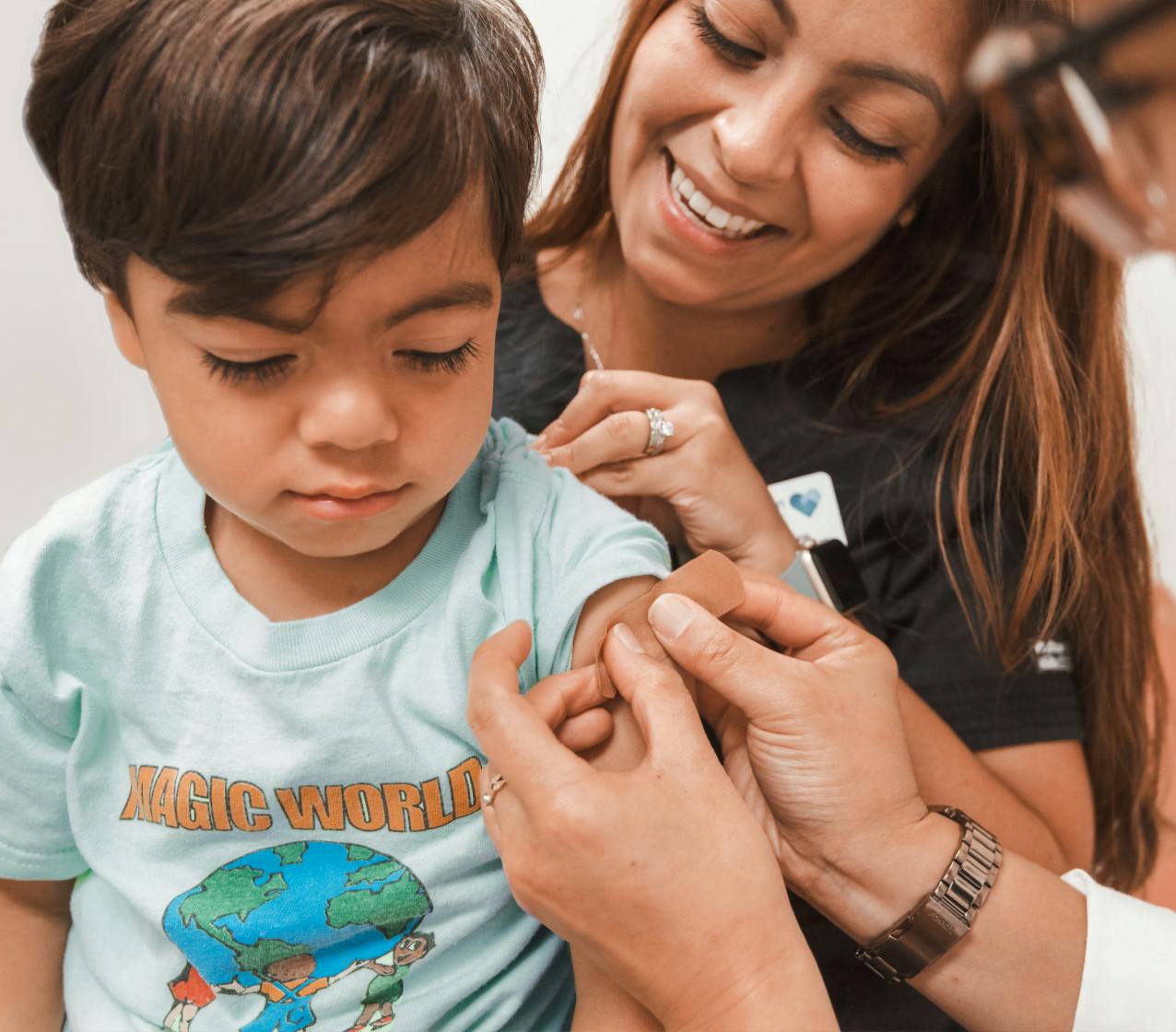 Kid gets flu shot and a bandage by a healthcare professional while on mother’s lap.