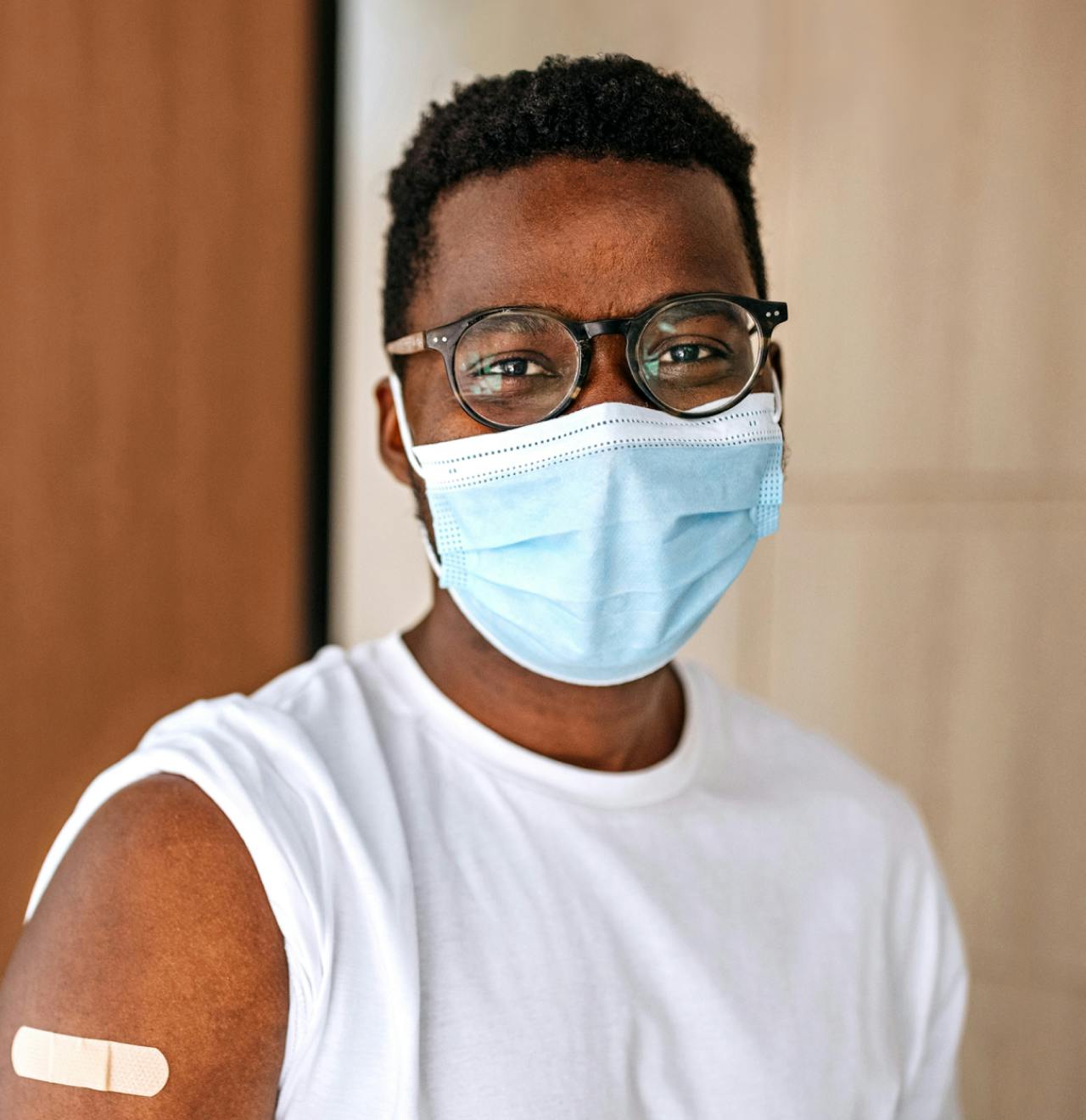 Person with a face mask and glasses has a rolled up sleeve and bandage after getting a flu shot.