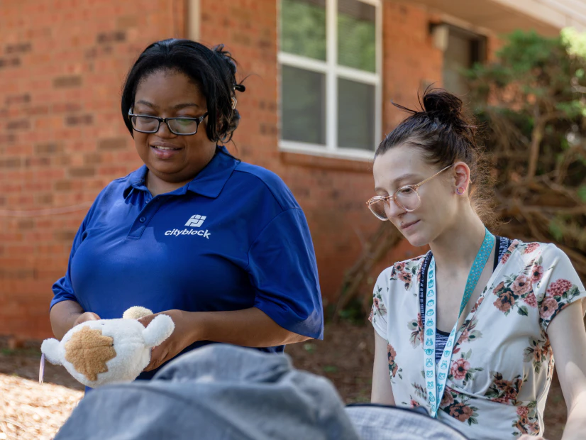 Image of a community health partner in a blue Cityblock polo walking with a member pushing a stroller outdoors.