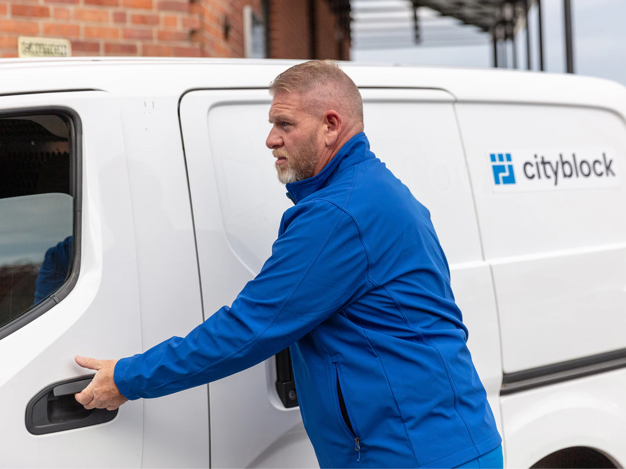 Image of a clinician in a blue jacket opening the driver's side door of a white Cityblock van parked outside a building.