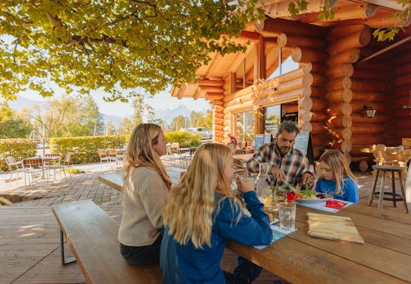Familie isst zu Mittag im Garten vom Restaurant Blockhouse - Camping Alpenblick
