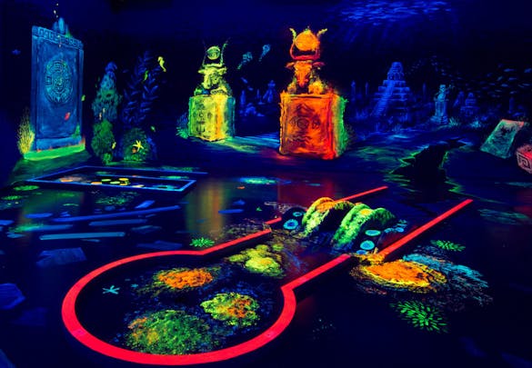 Dark indoor mini golf course with neon obstacles