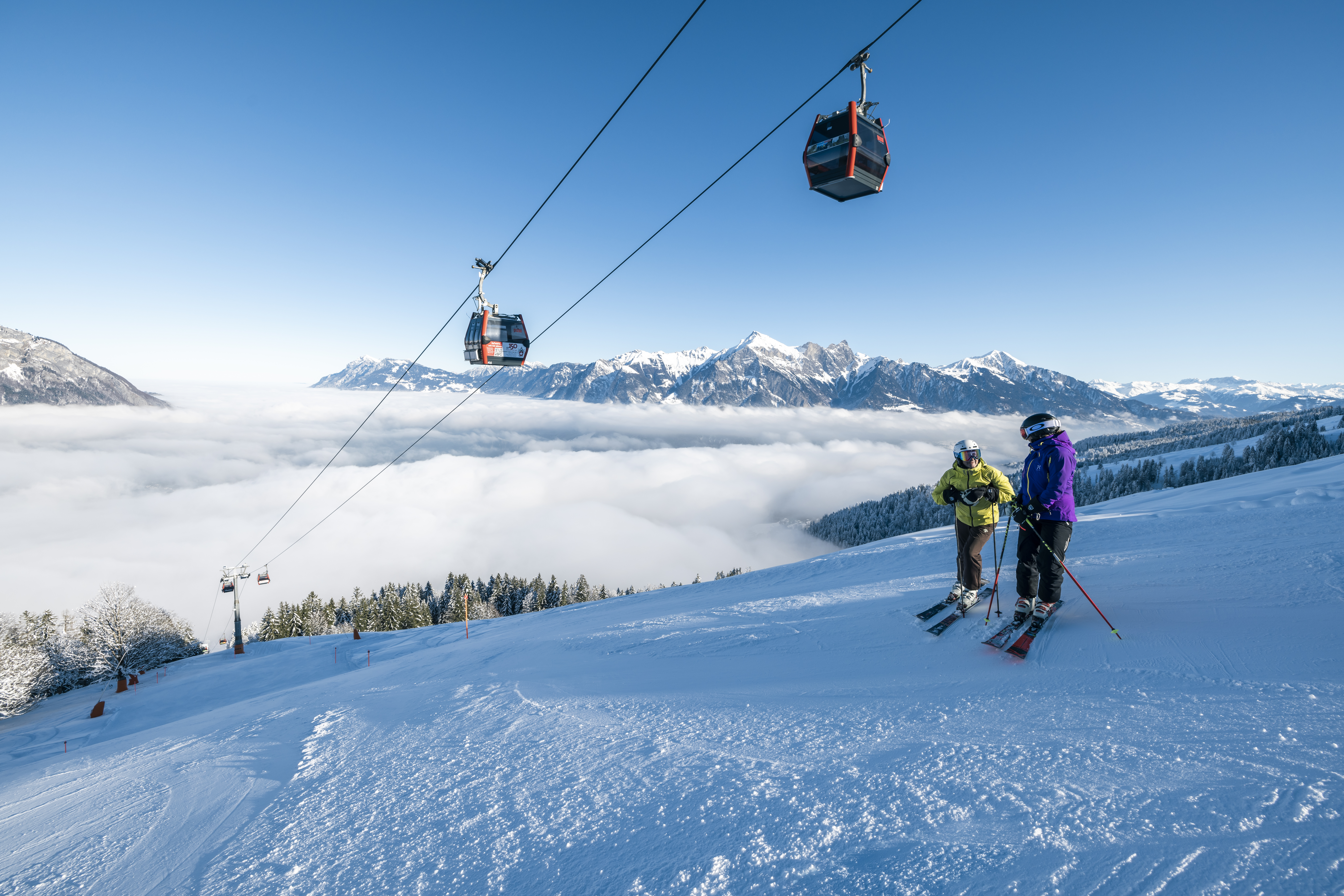 Zwei Skifahrer auf der Piste im Pizol Skigebiet mit Gondelbahn über ihnen und schönem Wetter