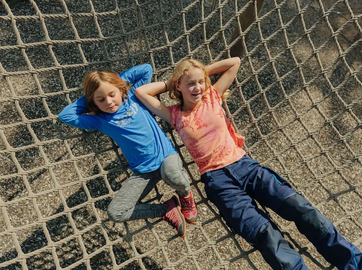 Zwei Kinder, die in einem Netz auf einem Spielplatz liegen