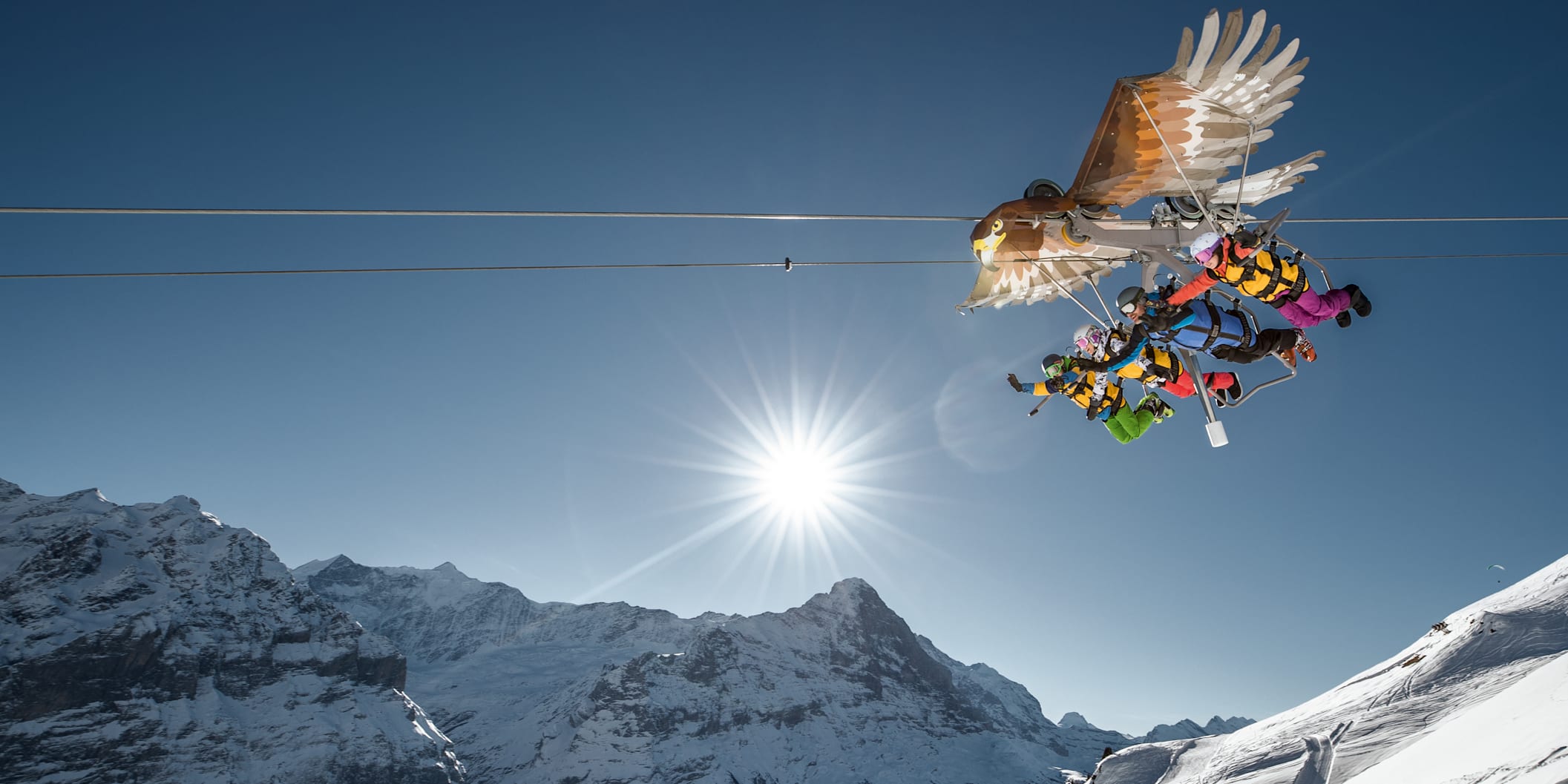 vier Personen auf einer Zip-Line im Winter mit Winterkleidung und Helmen, die den First Glider hinunterfliegen