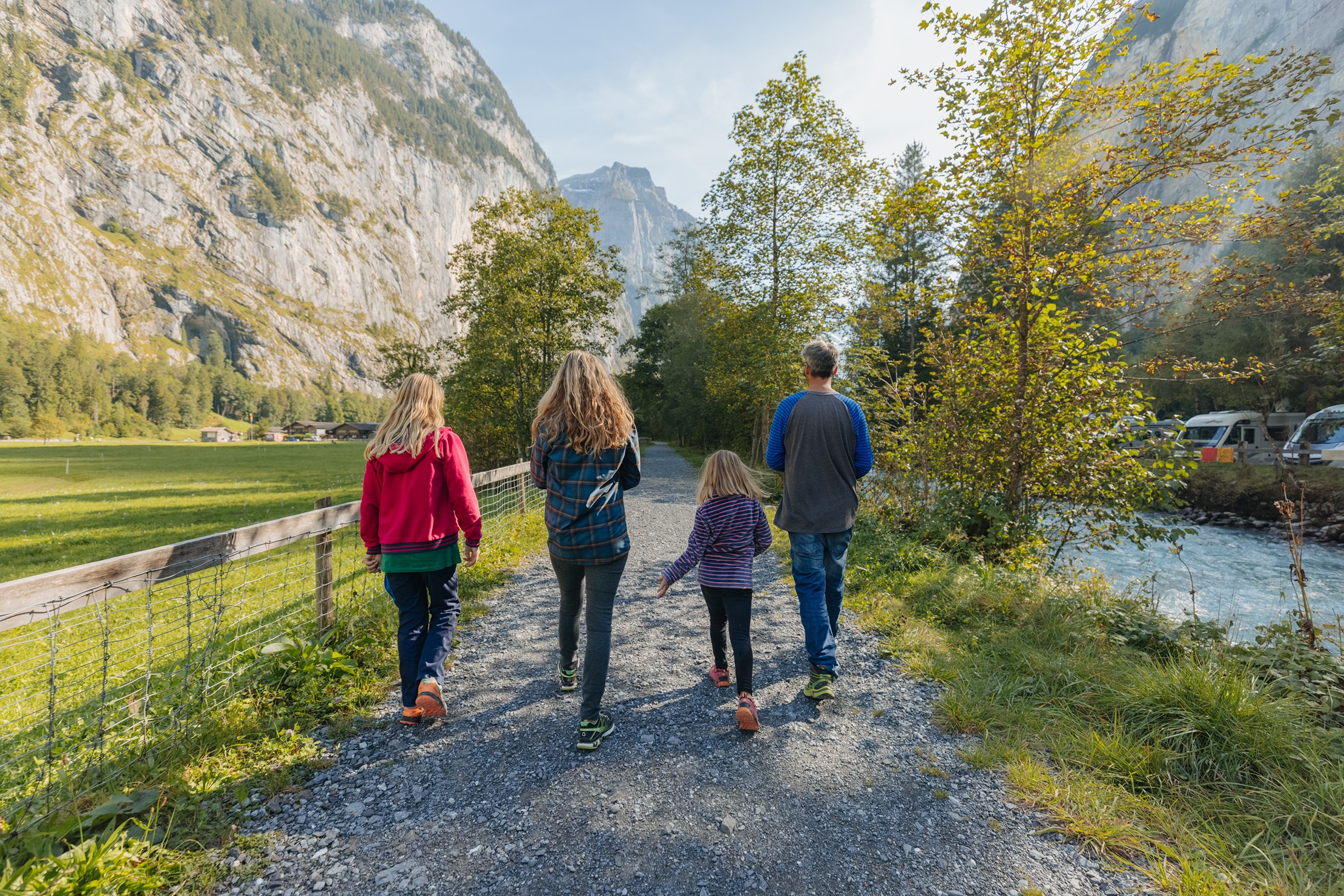Vierköpfige Familie spaziert entlang des Flusses, weisse Lütschine in Lauterbrunnen mit steilen Felswänden im Hintergrund 