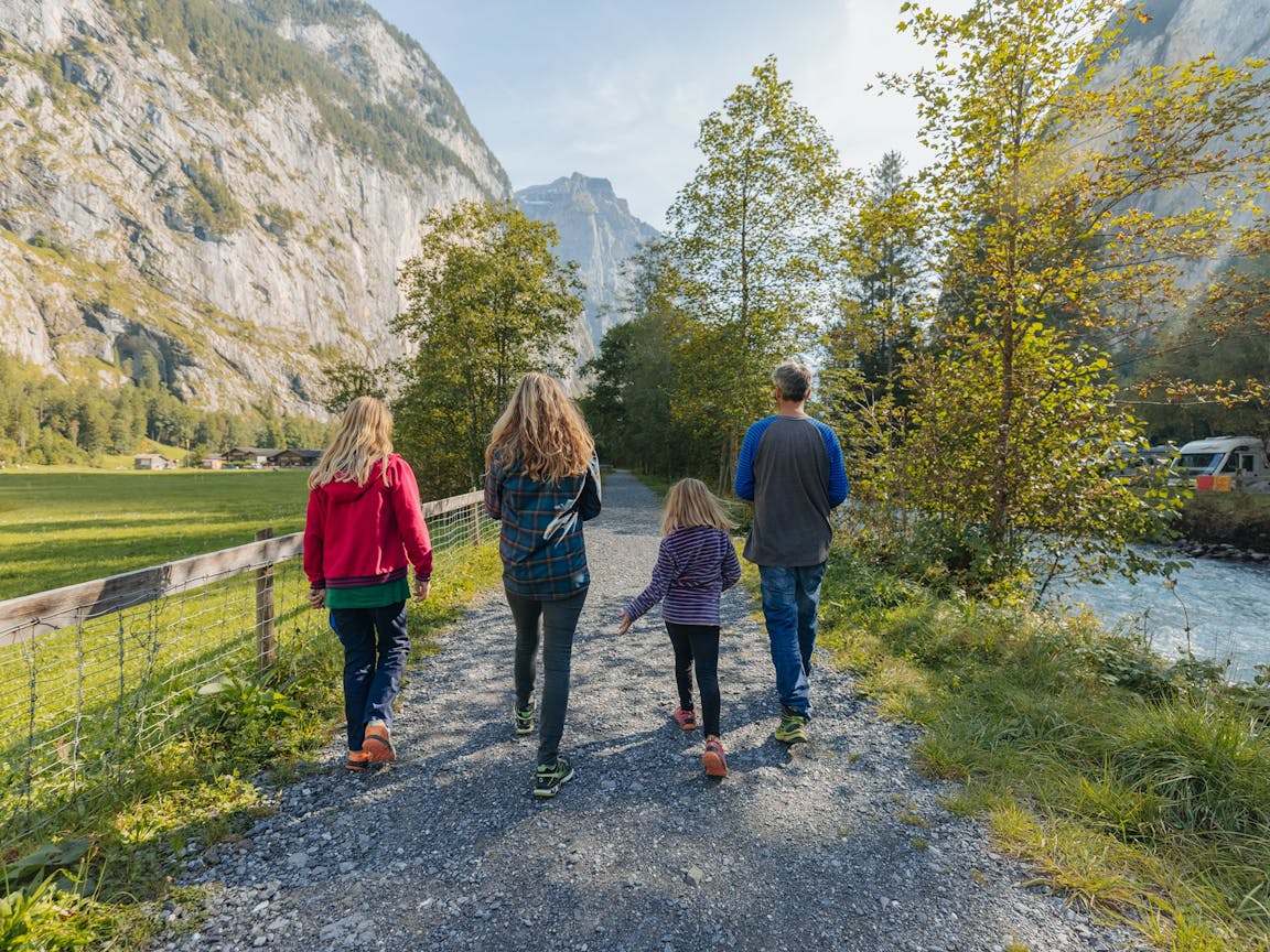 family of four walking nex to the river Weisse Lütschine in Lauterbrunnen with steep rock walls in the background