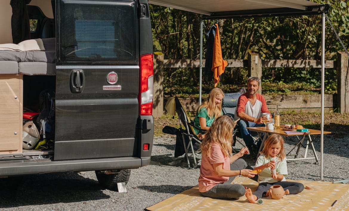 sprinter van on a pitch at Camping Jungfrau with a family sitting on a blanket and camping chairs