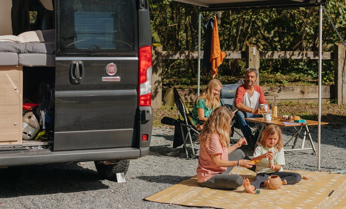Sprinter en una parcela del Camping Jungfrau con una familia en una manta y sillas de camping