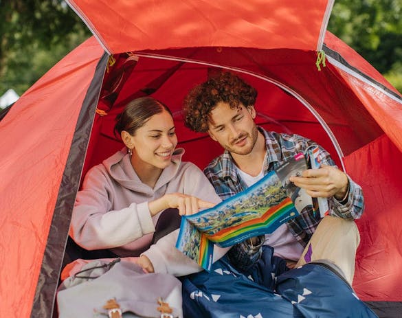 Ein Mann und eine Frau sitzen im Eingang ihres Zeltes und schauen sich den Lageplan des Campingplatzes an - Camping La Nouvelle Plage