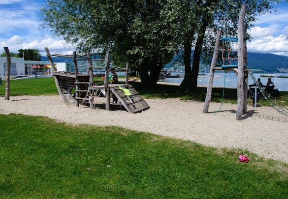 Kinderspielplatz am See Natur mit Bäumen Wiese und Sandstrand Neuenburger See Berge im Hintergrund
