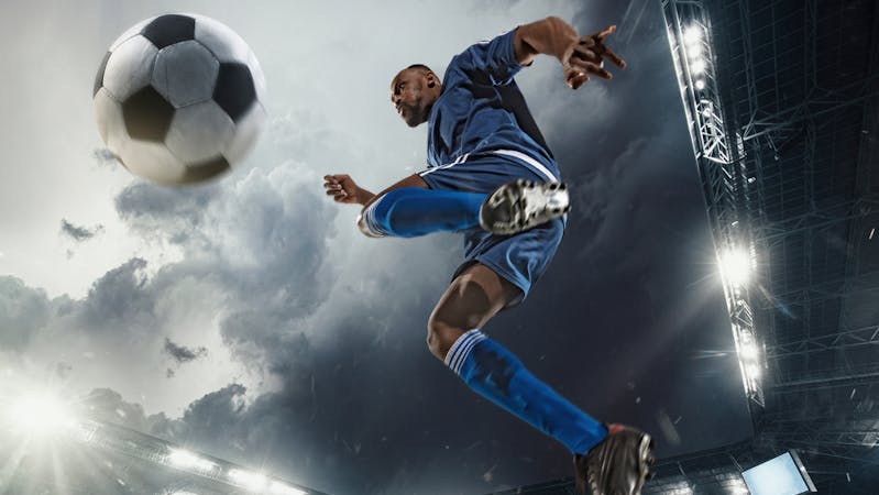 A football player hitting the ball in the stadium.