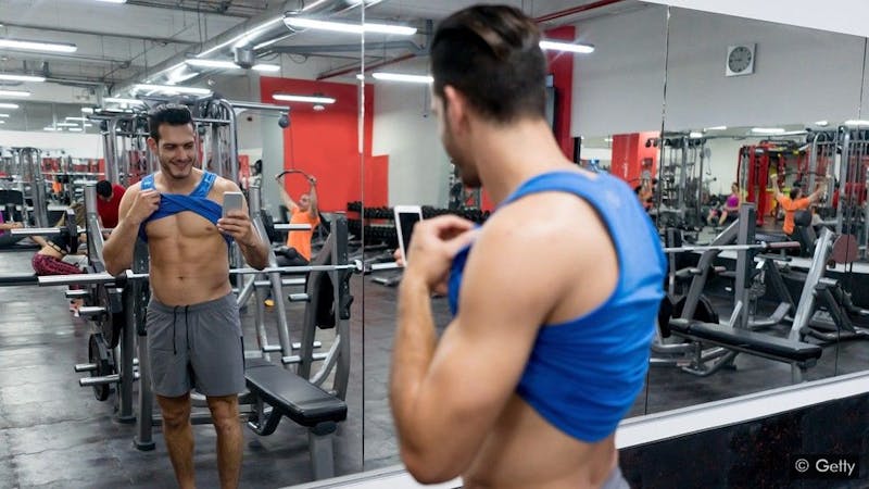 A young man taking a picture showing his six-packs at the gym