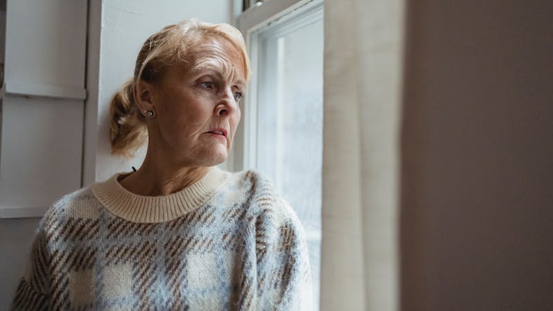 An elderly woman in her menopausal years looking through her window to the outside