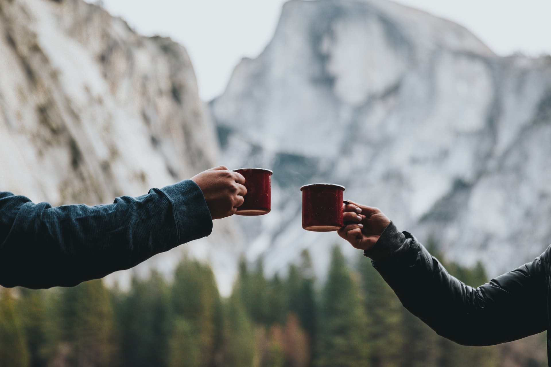Two arms coming from both side to meet with their mugs in the center with mountains in the background