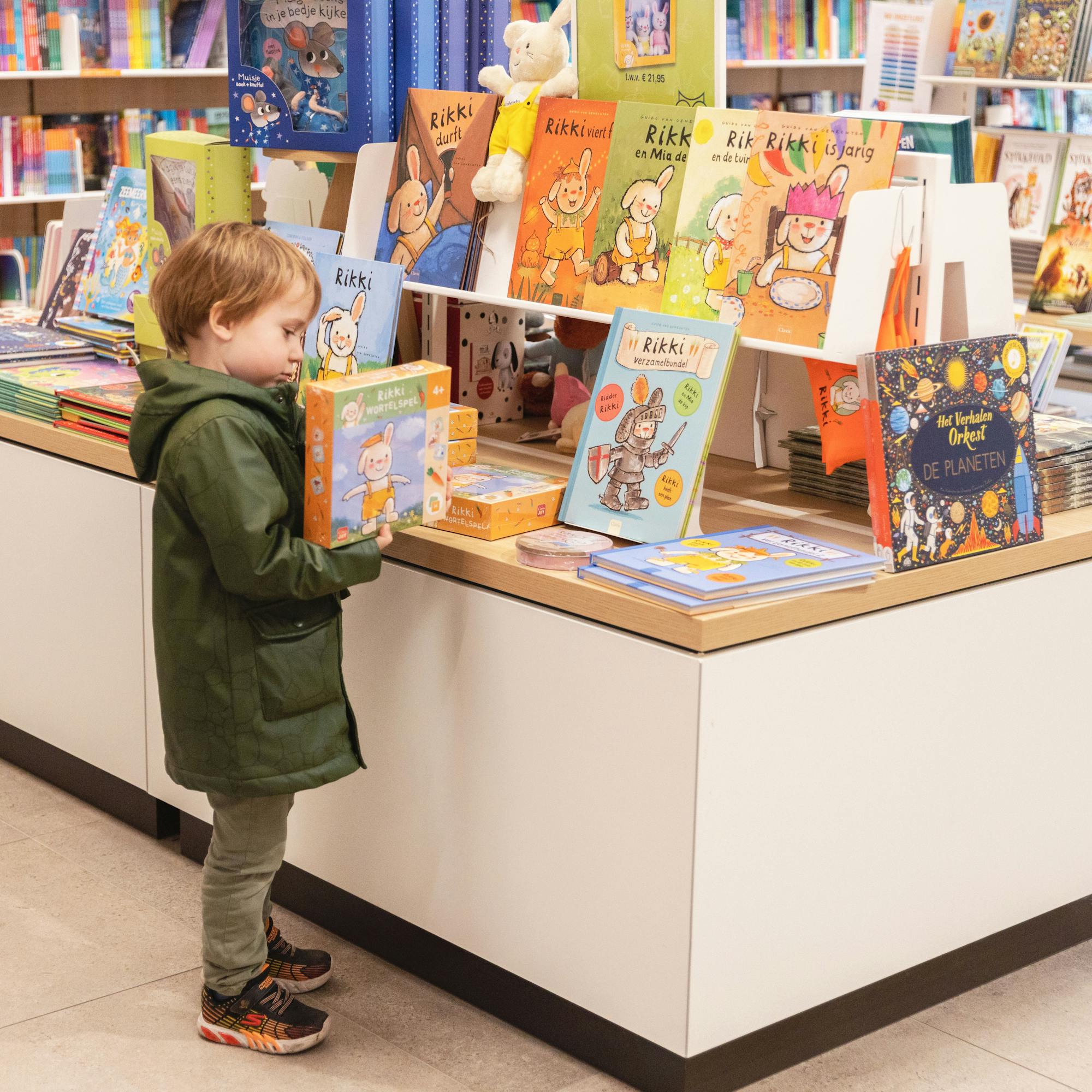 Een kindje bekijkt het Rikki wortelspel in de Standaard Boekhandel. Het spel ligt aan een Rikki-rek waarop alle Rikki producten en boeken liggen uitgestald/ 