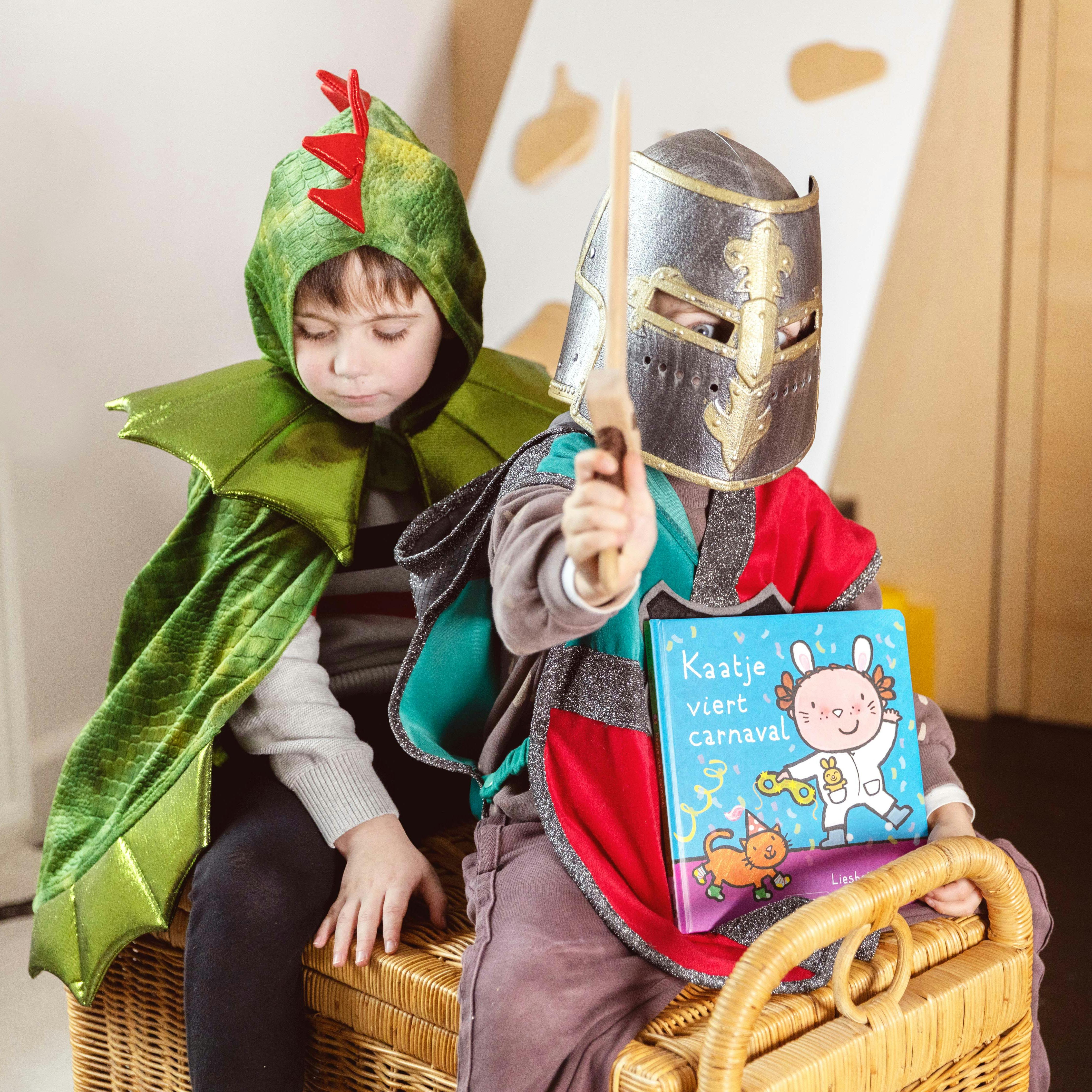 Foto van twee kleuters op een verkleed als draak en ridder op een verkleedkoffer met het carnavalsboek Kaatje viert carnaval van Liesbet Slegers.