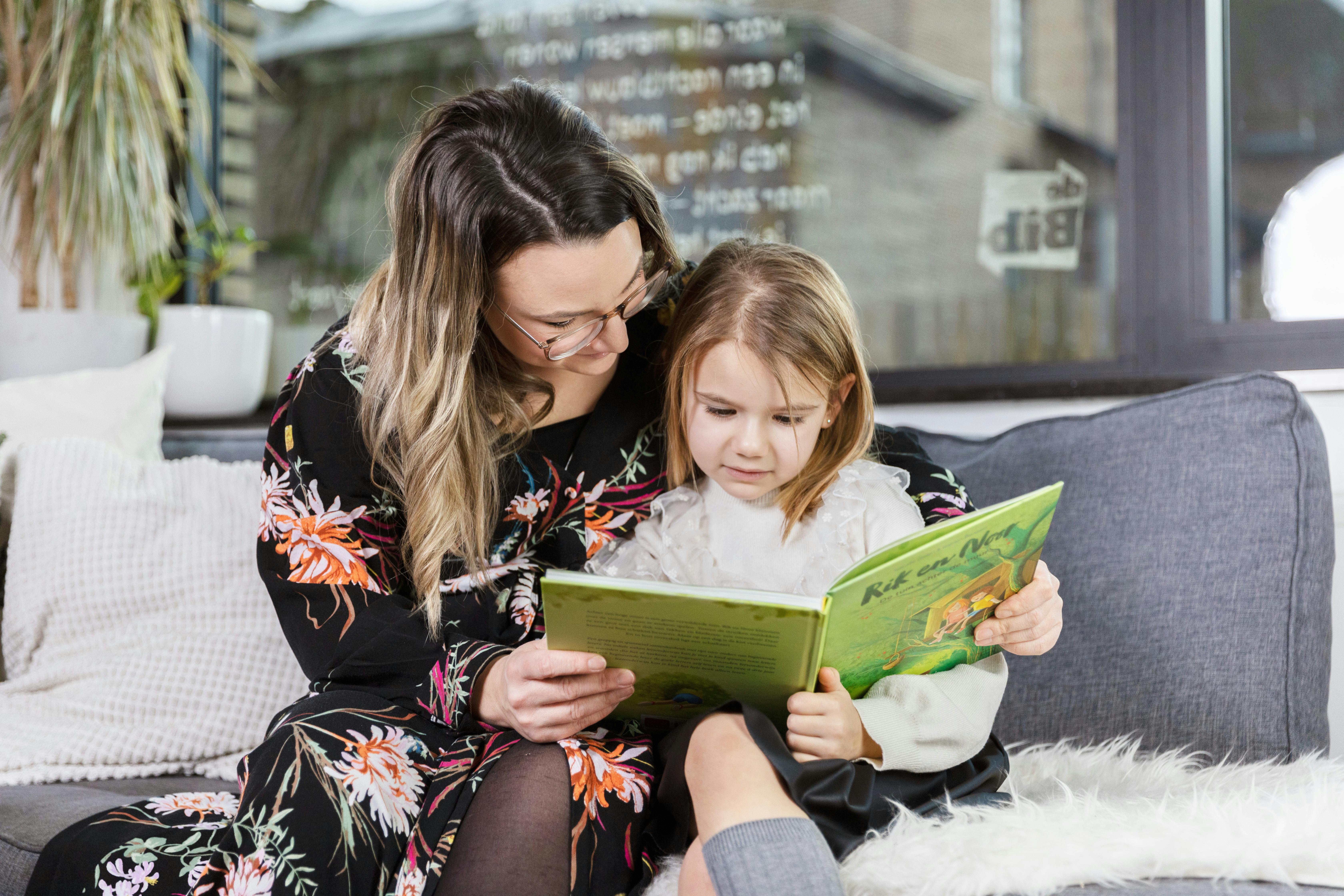 Foto waarop een mama samen met haar dochtertje in de zetel een boek leest.