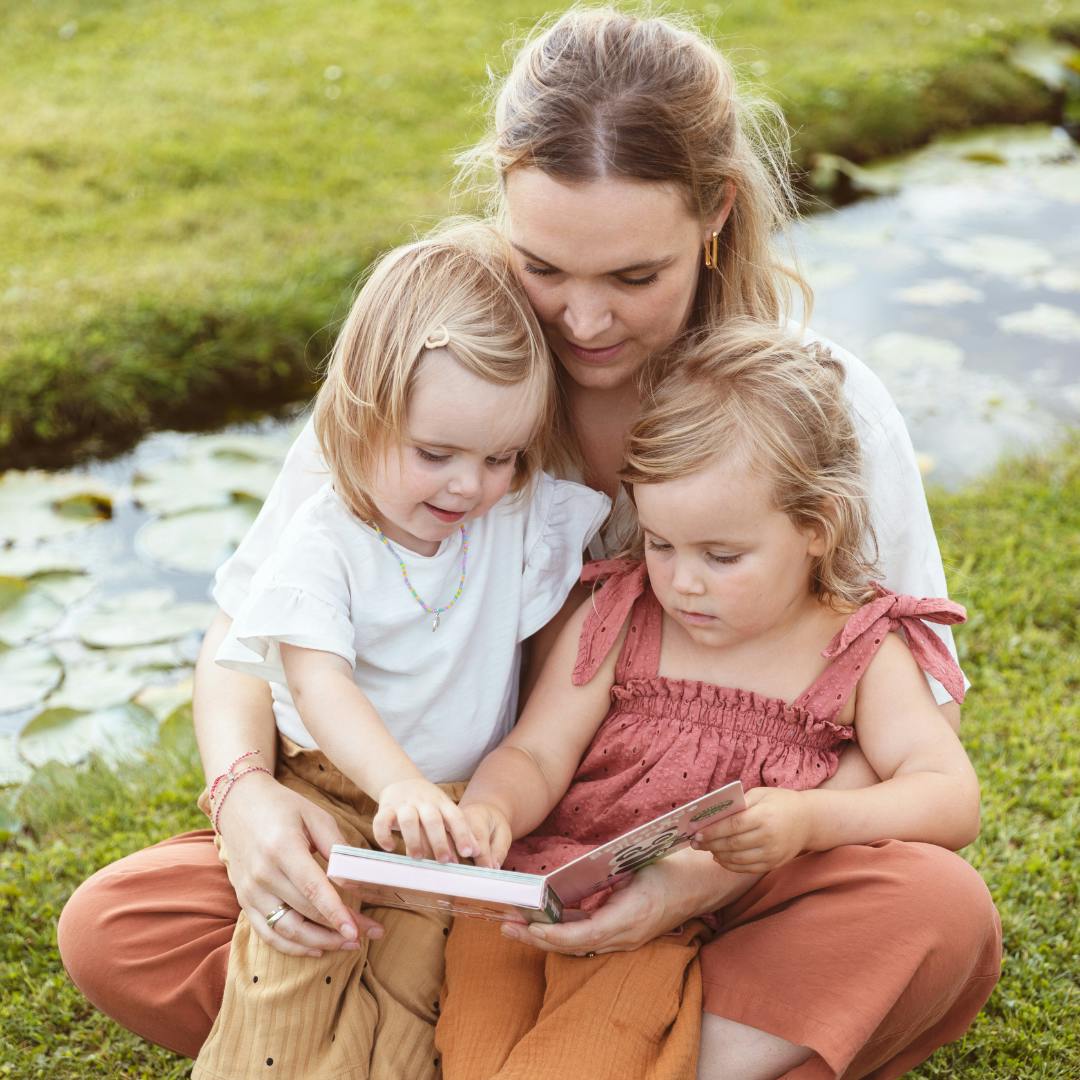 Lentekriebels. Een mama leest samen met haar twee peuters een boekje in de tuin. 