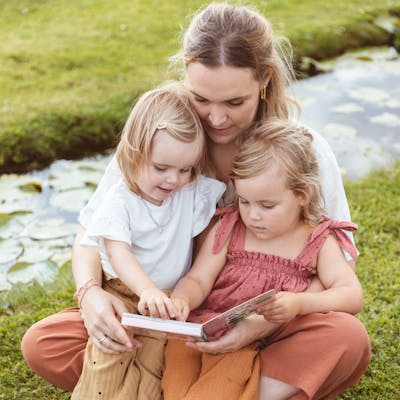 Lentekriebels. Een mama leest samen met haar twee peuters een boekje in de tuin. 