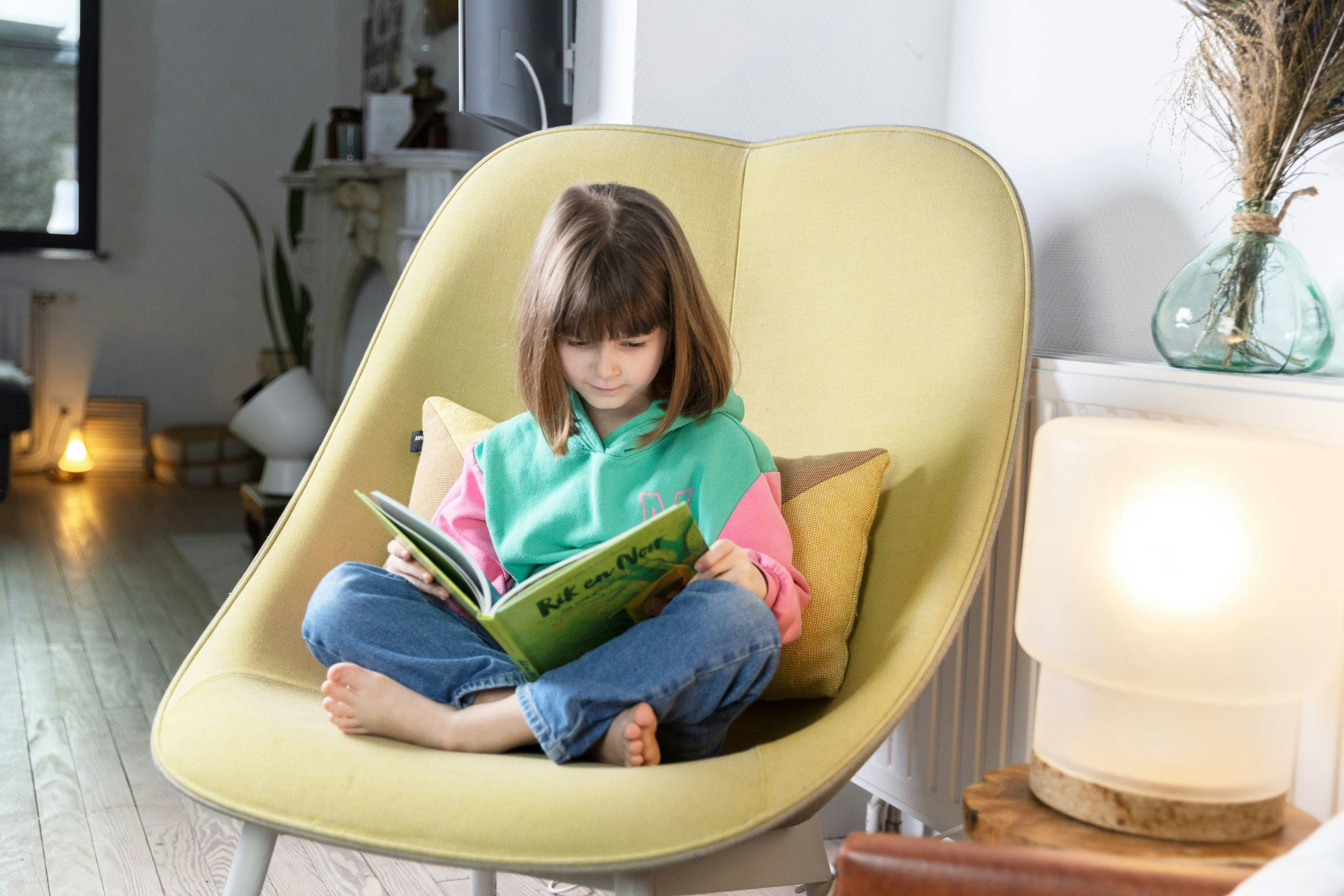 Meisje met bruine haren leest een boek in een gele zetel