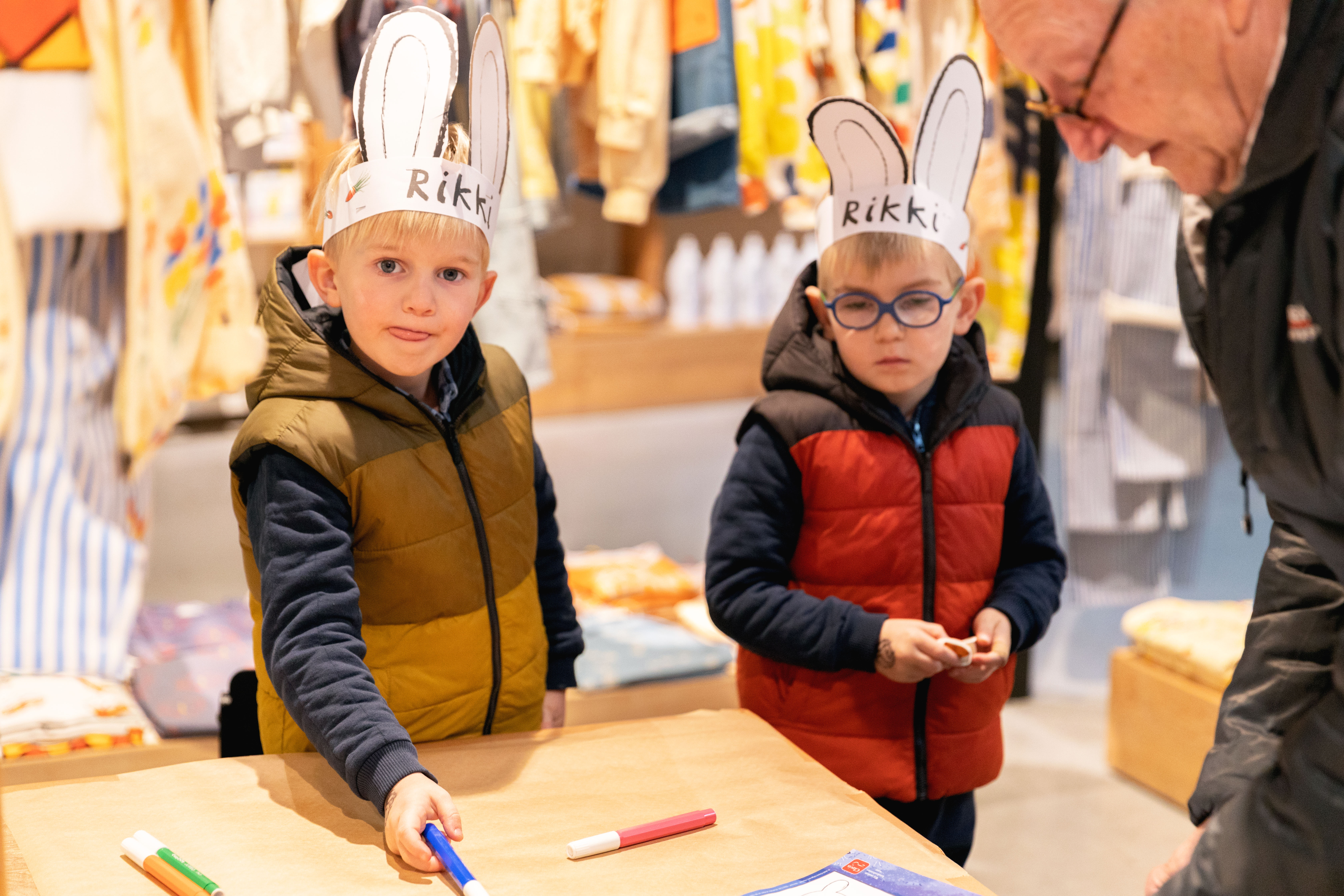 Twee jongens met Rikki-oortjes op hun hoofd. Ze kleuren samen met hun opa een Rikki-raket in. 