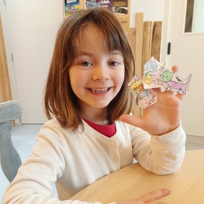 Een meisje toont blij haar zelf geknutselde vingerpopjes van Rikki. De vinderpopjes van papier zitten op haar linker hand. Deze foto werd genomen op de Rikki belevingsnamiddag in Brugge. 