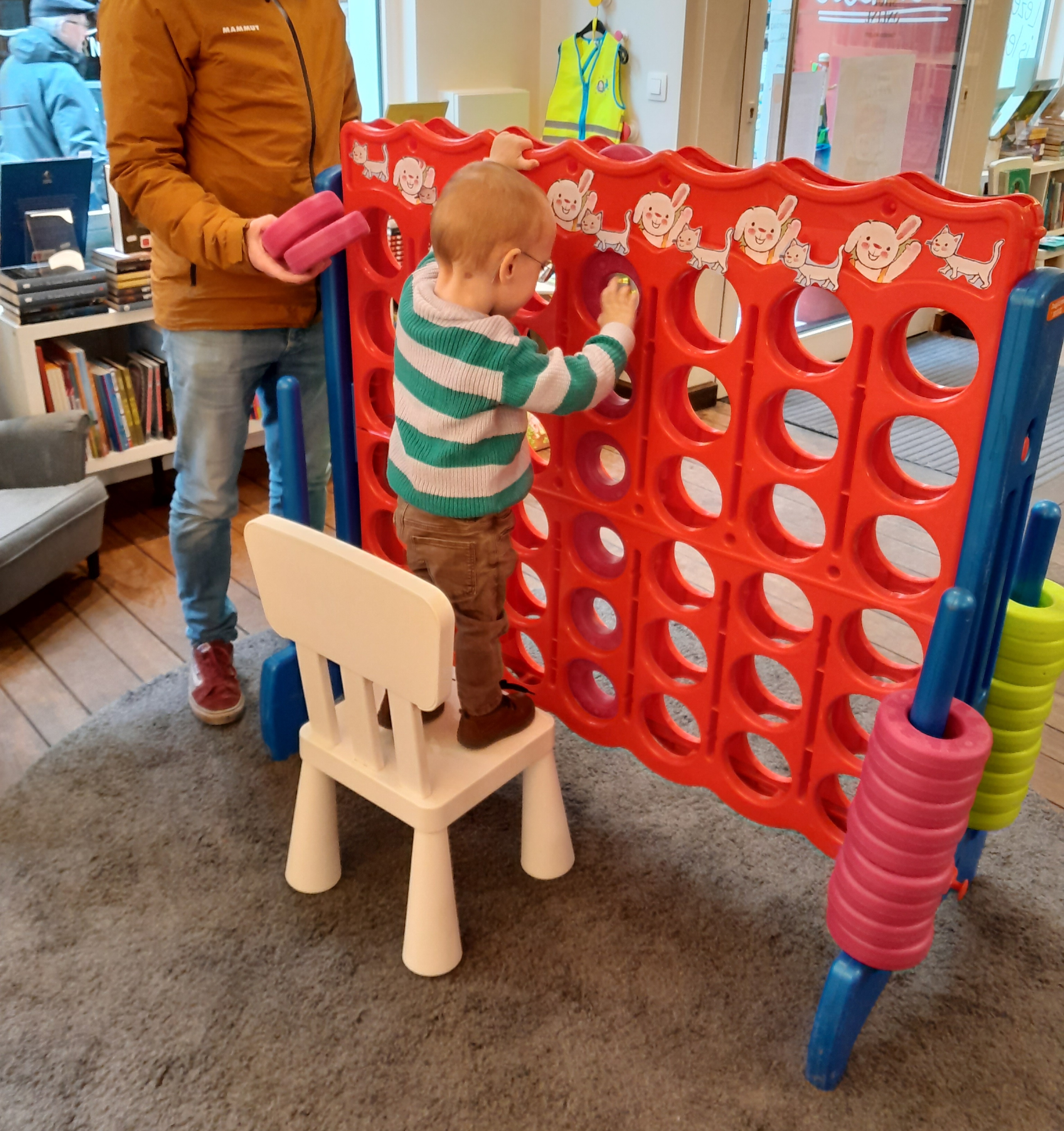 Een kindje staat op een stoel om 'vier-op-een-rij' te spelen.