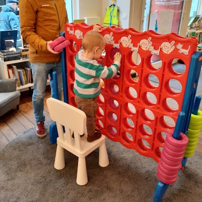Een kindje staat op een stoel om 'vier-op-een-rij' te spelen.