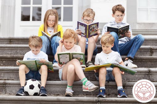 Zes kinderen zitten buiten op een trap een boek te lezen.