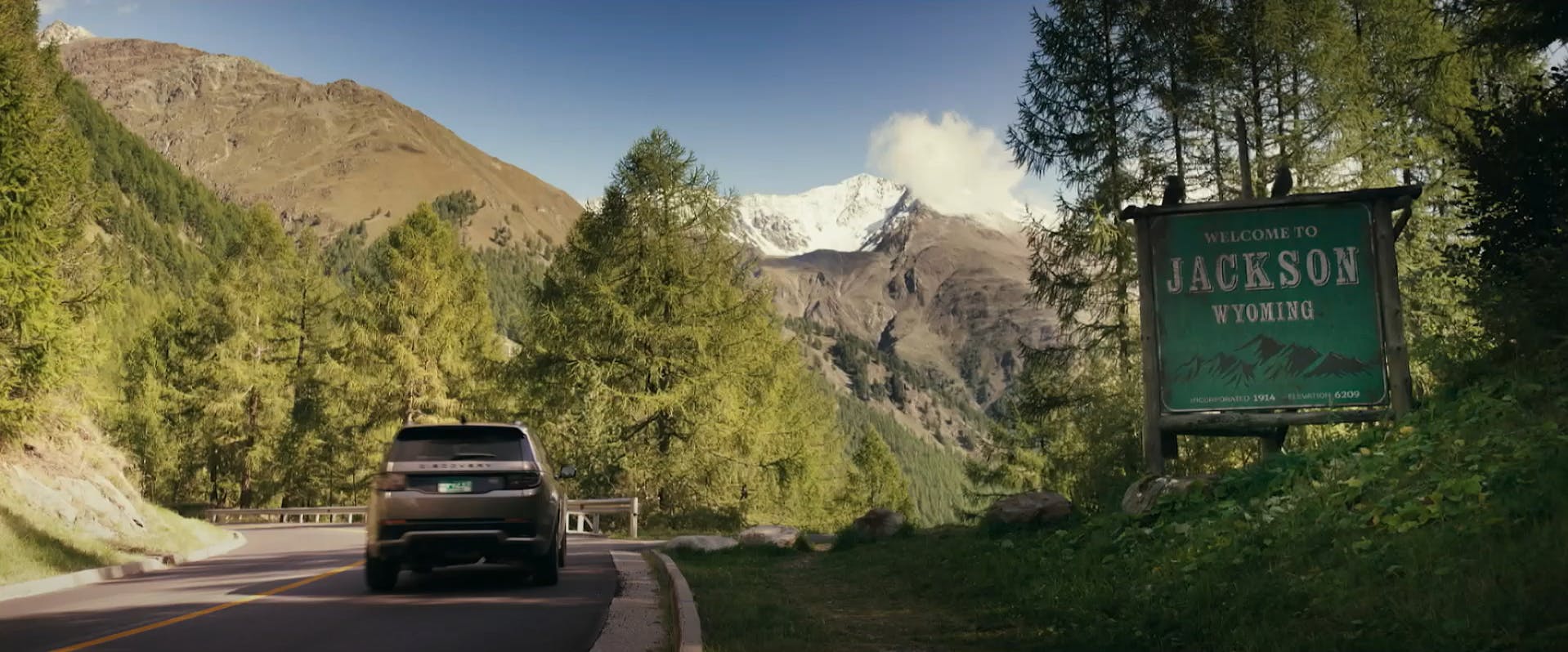 Het openingsshot van de trailer van Woodwalkers. Een auto rijdt op een weg in de bergen en passeert een bord met 'welcome to Jackson, Wyoming'.