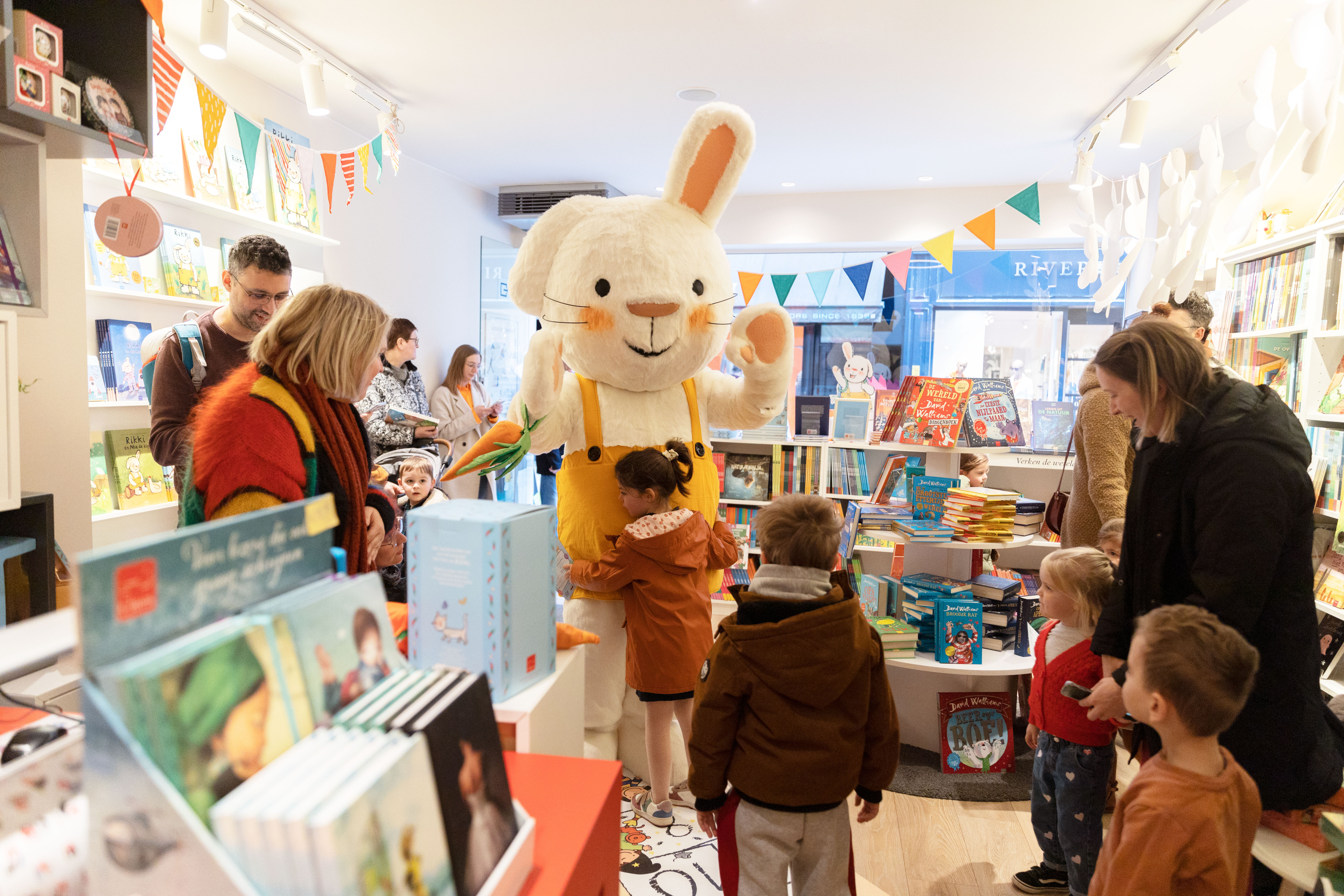 Een foto van Rikki in de Clavis Conceptwinkel in Hasselt. Rikki krijgt een knuffel van een meisje en er staan nog andere kinderen rond Rikki om samen met hem op de foto te kunnen