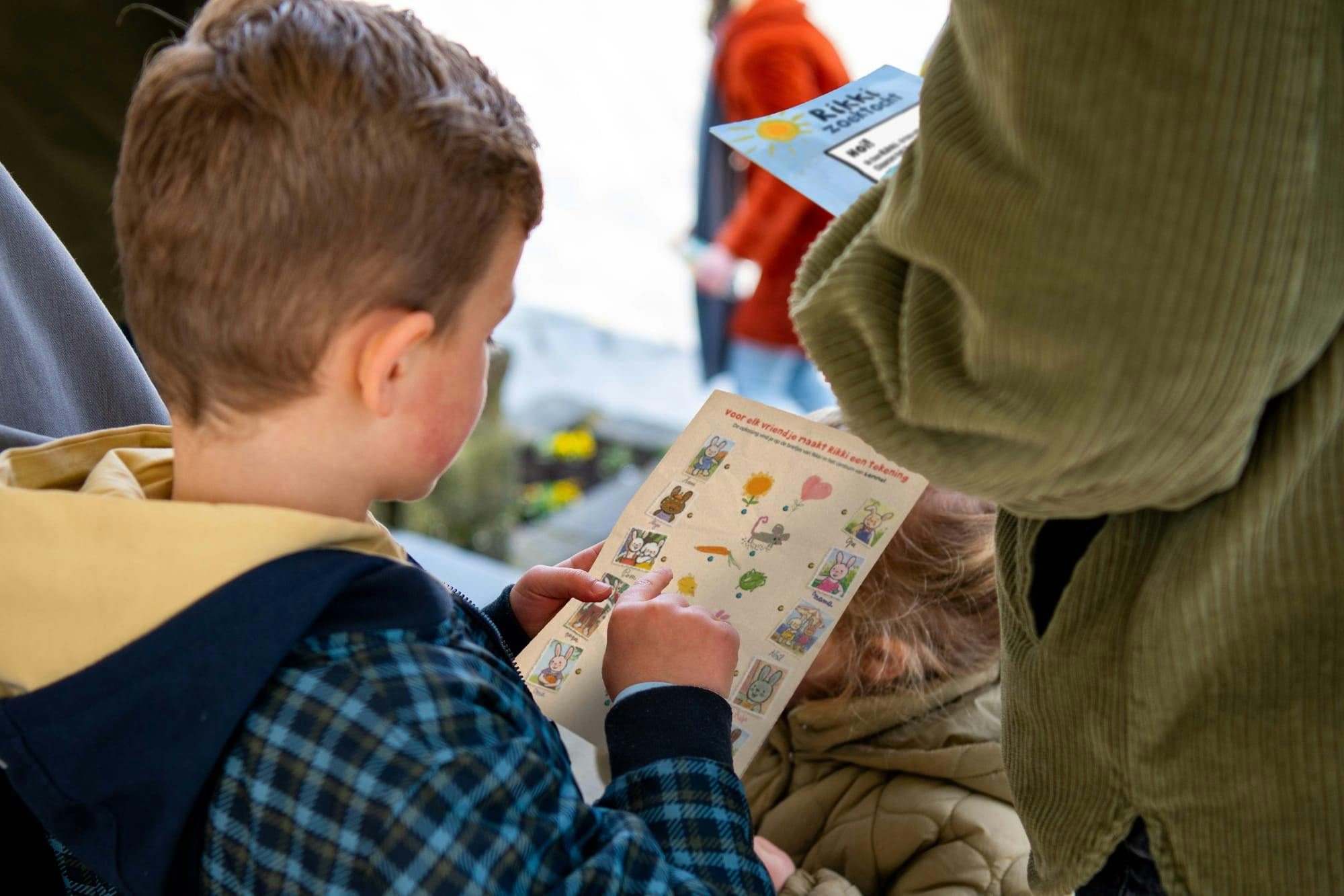 foto van jongen die zoektocht doet en met zijn vinger op een opdrachtblaadje wijst
