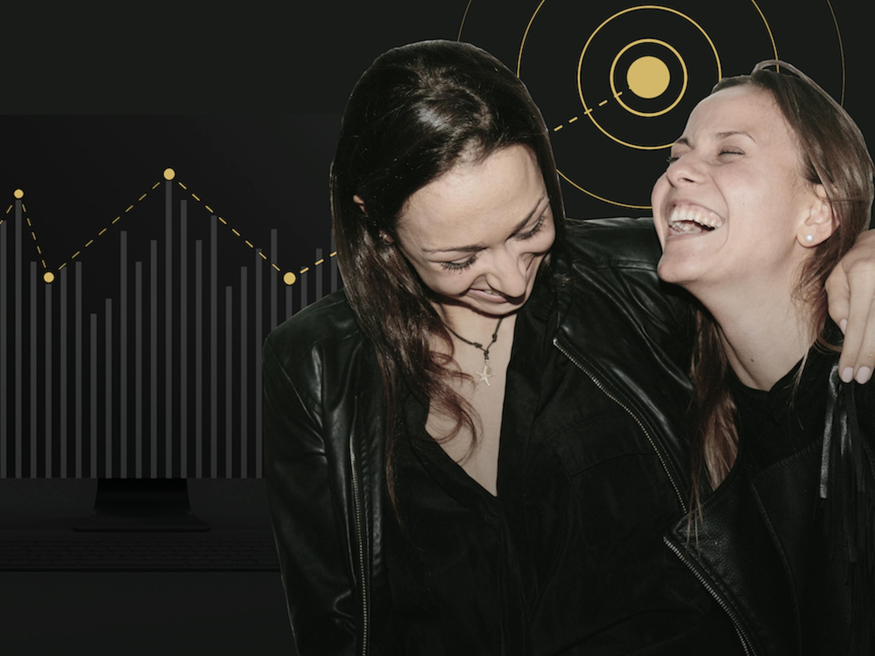 Two women laugh with their arms around each other in front of a graph showing positive growth.