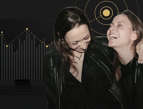 Two women laugh with their arms around each other in front of a graph showing positive growth.