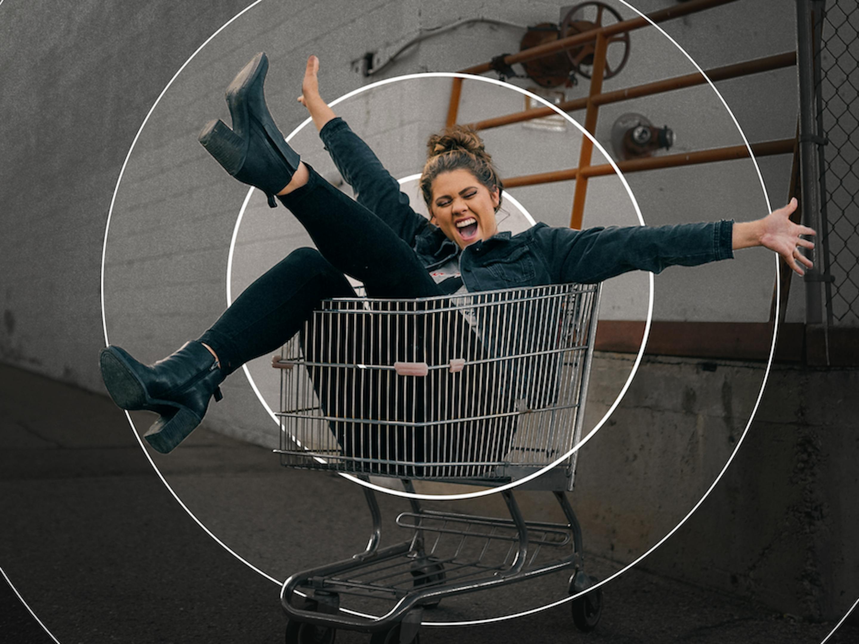 A woman cheers and kicks her leg up while sitting in a shopping cart