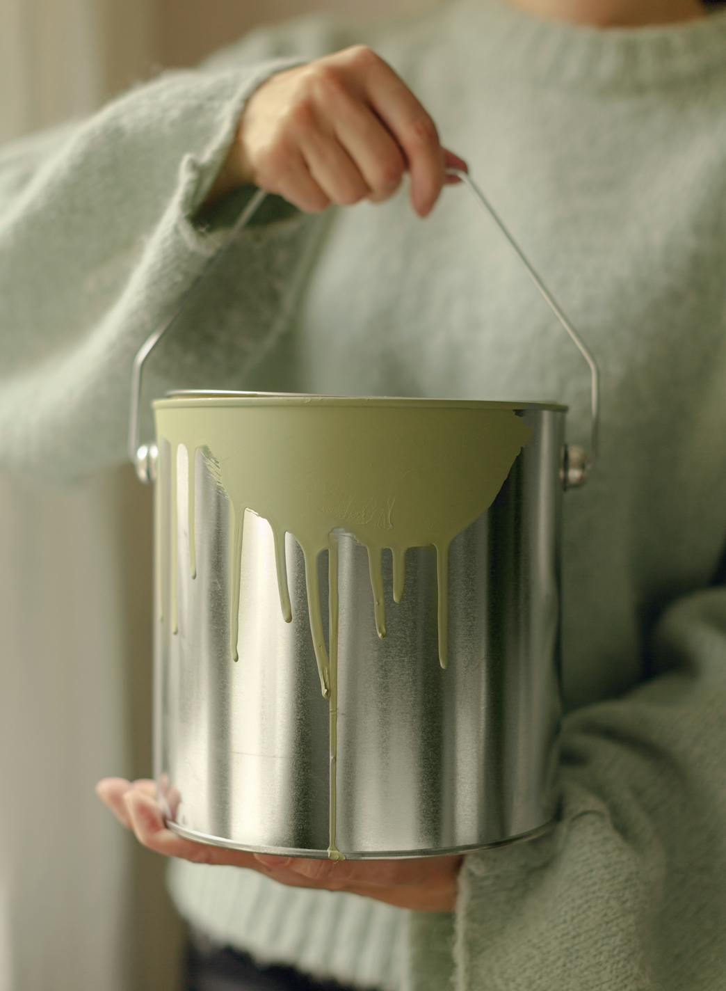 A woman holds a paint can in front of her torso. Green paint spills out