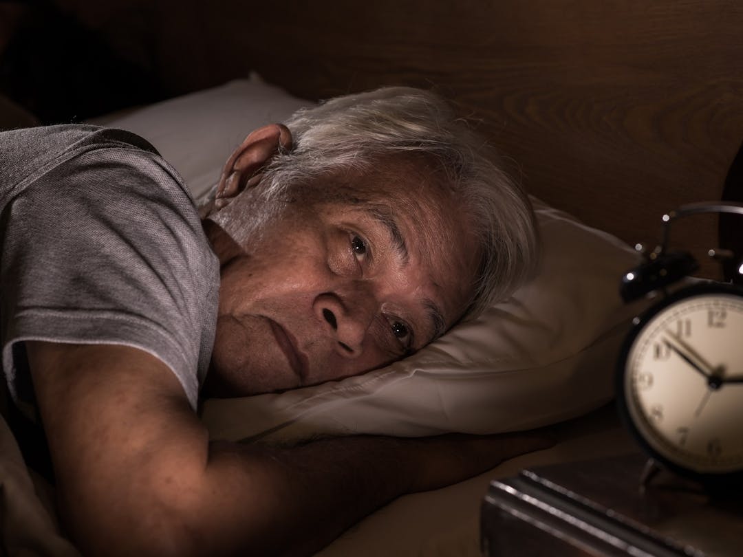 An older man lies awake in bed in the middle of the night