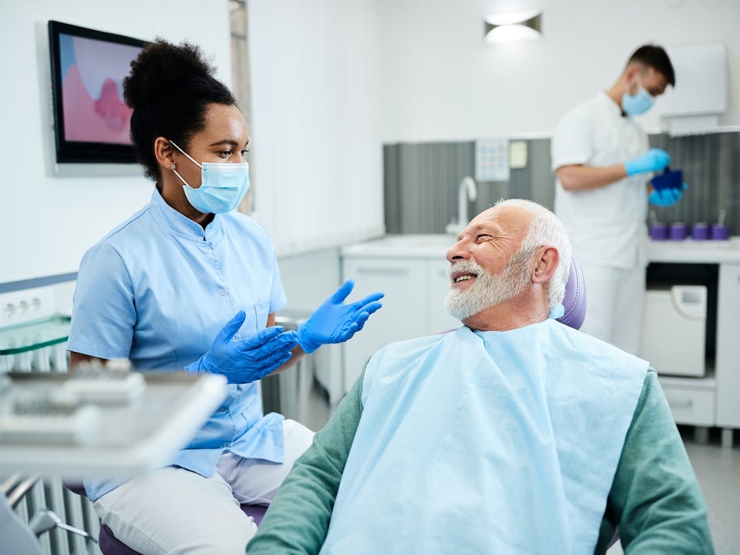 A male patient in a dental chair with a female dentist explaining a procedure