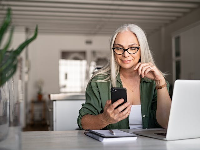 Woman on laptop looking at her phone