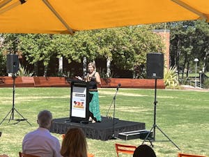 Dr Vanessa Rauland standing on a low stage with a podium, in a garden delivering her speech.