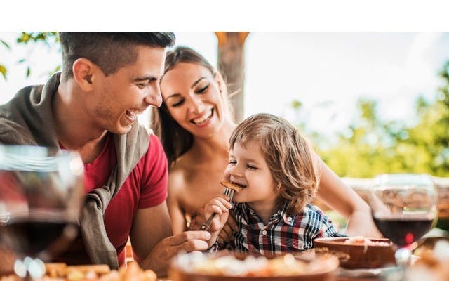 child eating food at restaurant with his parents