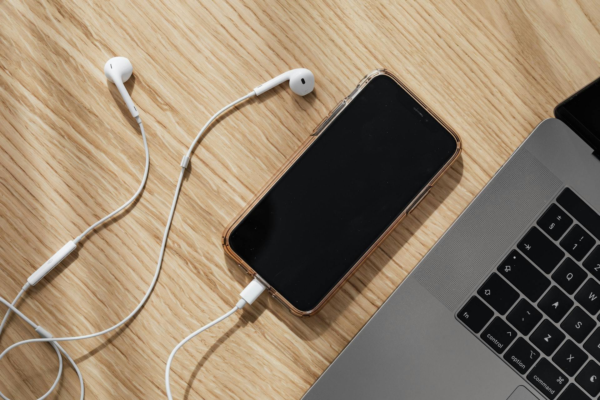 cell phone plugged into earbuds next to laptop
