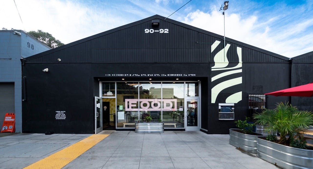 A black facility with white details, a big window and a glass door on the center, on the back the sky is blue and there are a few clouds