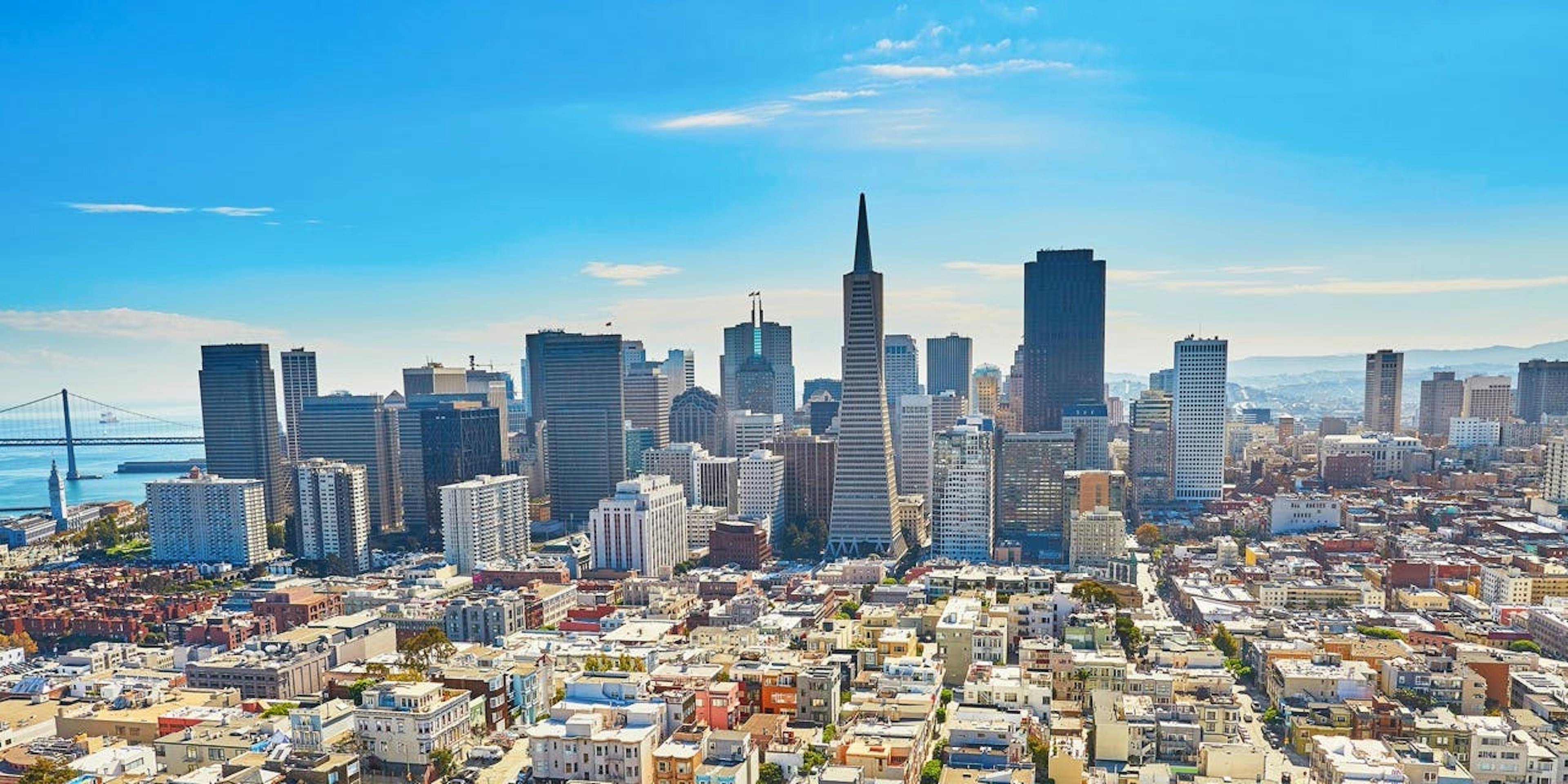 Aerial vision of San Francisco with an area of high buildings and another with smaller builings, on the back is the Golden Gate bridge, a blue sky and a few clouds
