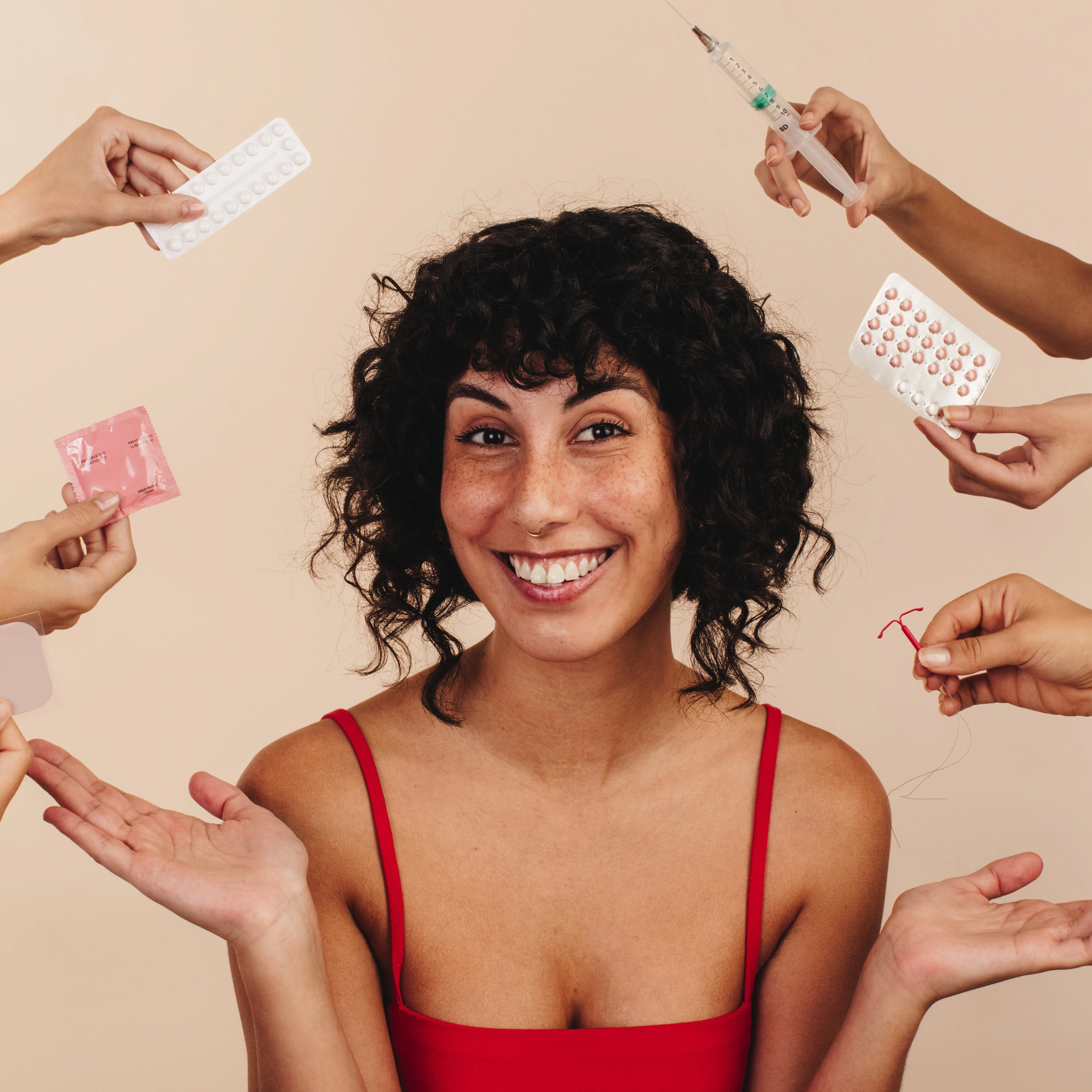 A woman is smiling with an assortment of birth control options surrounding her. 